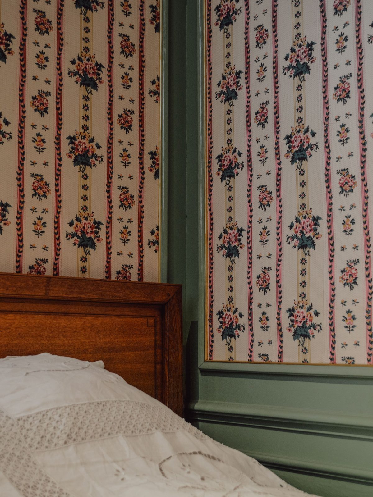 Bedroom corner with floral striped wallpaper, sage green trim and a wooden bed frame