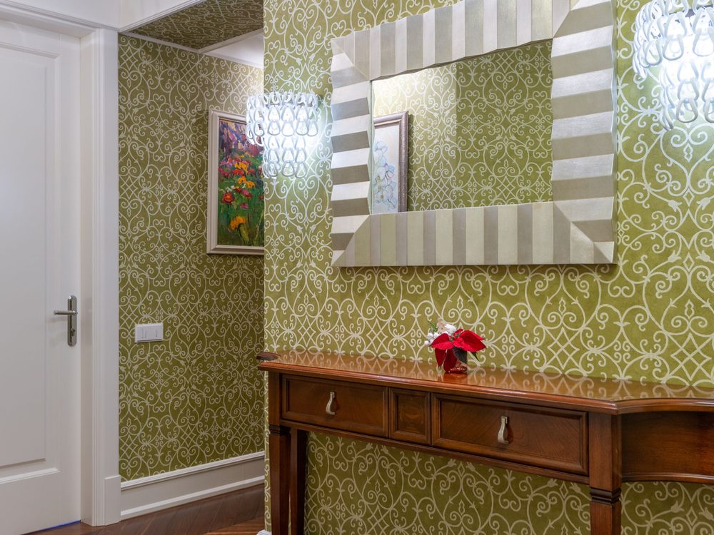 Sophisticated hallway with green-and-cream trellis wallpaper, a striped mirror and a wooden console