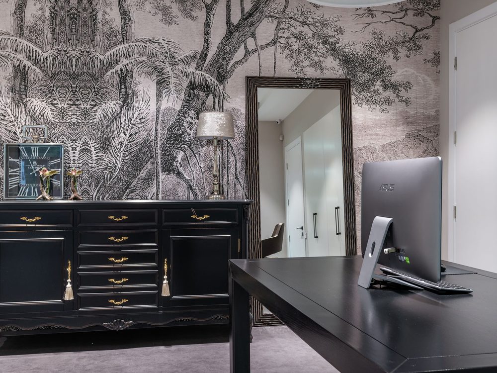 Home office with a soft grey landscape mural wallpaper behind a black desk and dresser