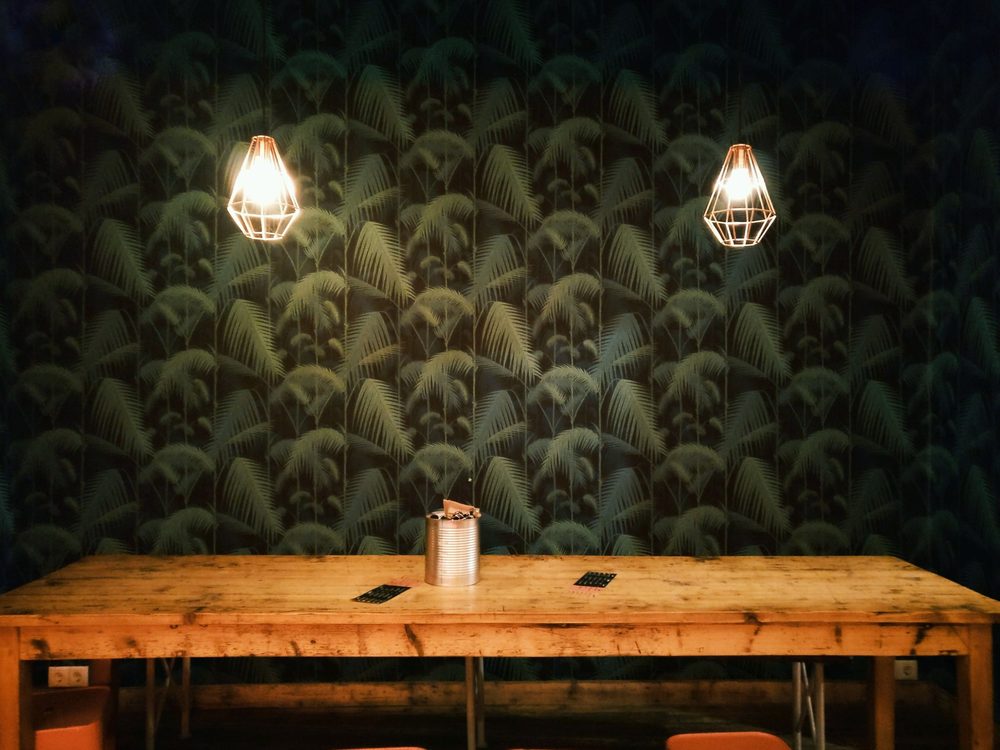 Dining room with dark green palm-leaf wallpaper, a rustic wood table and pendant lights