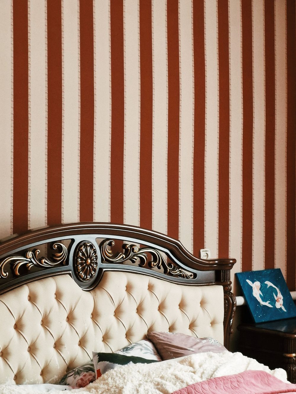 Traditional bedroom with rust-and-cream striped wallpaper behind a tufted headboard