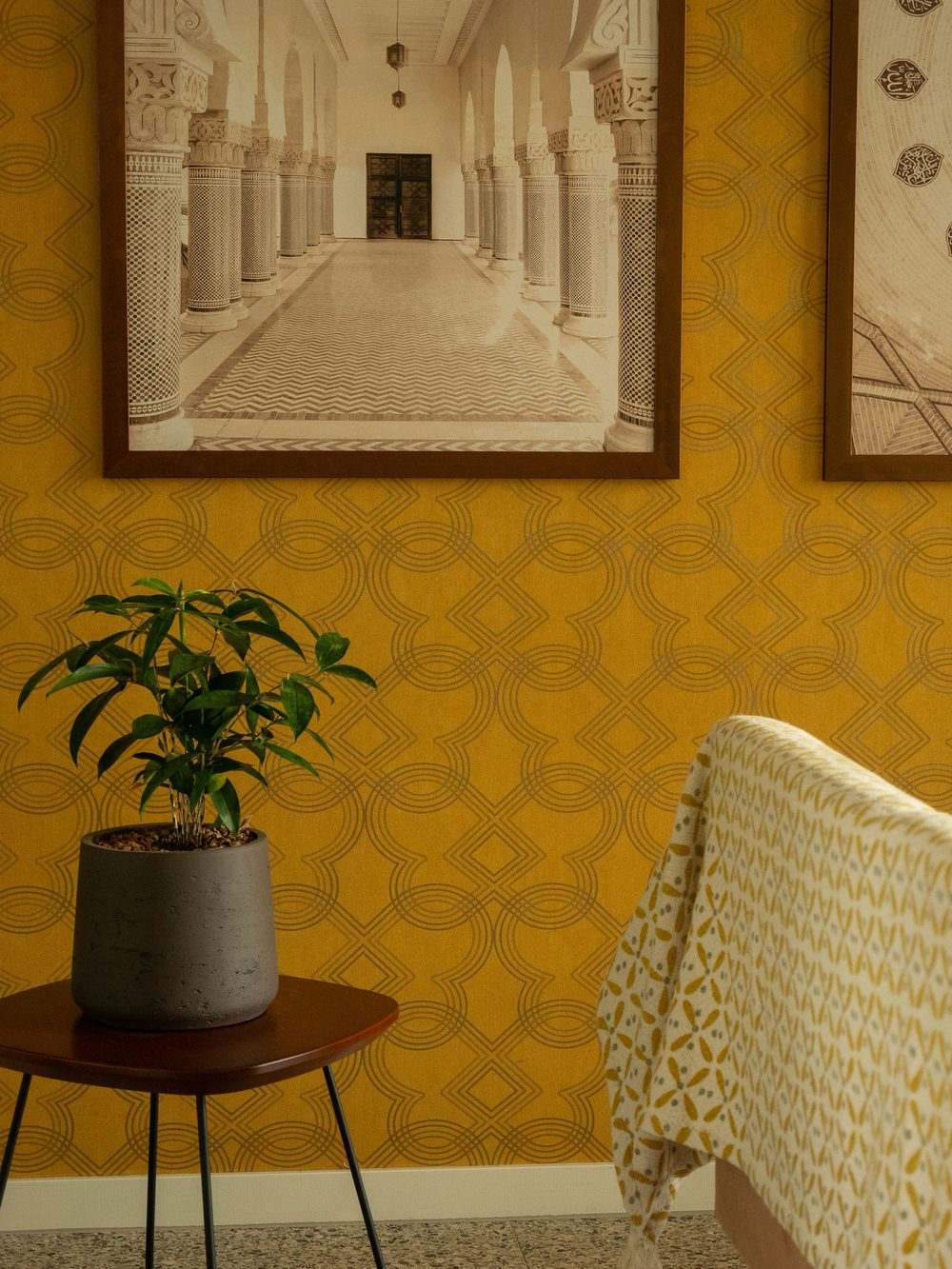 Living room corner with mustard geometric wallpaper, framed architectural prints and a potted plant