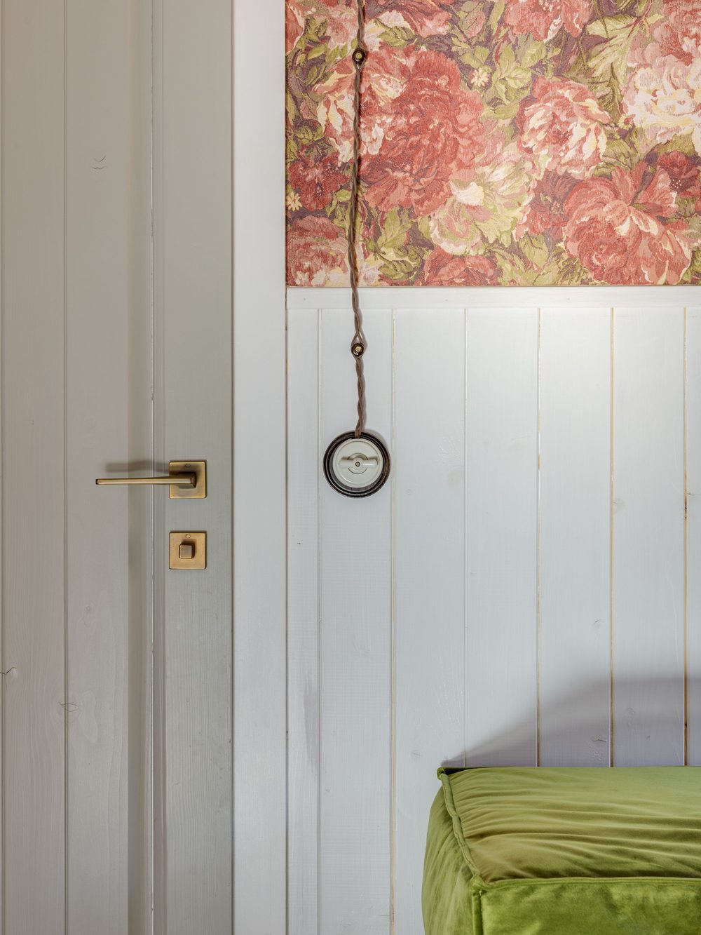 Rose floral wallpaper above white painted wainscoting beside a door with a brass handle
