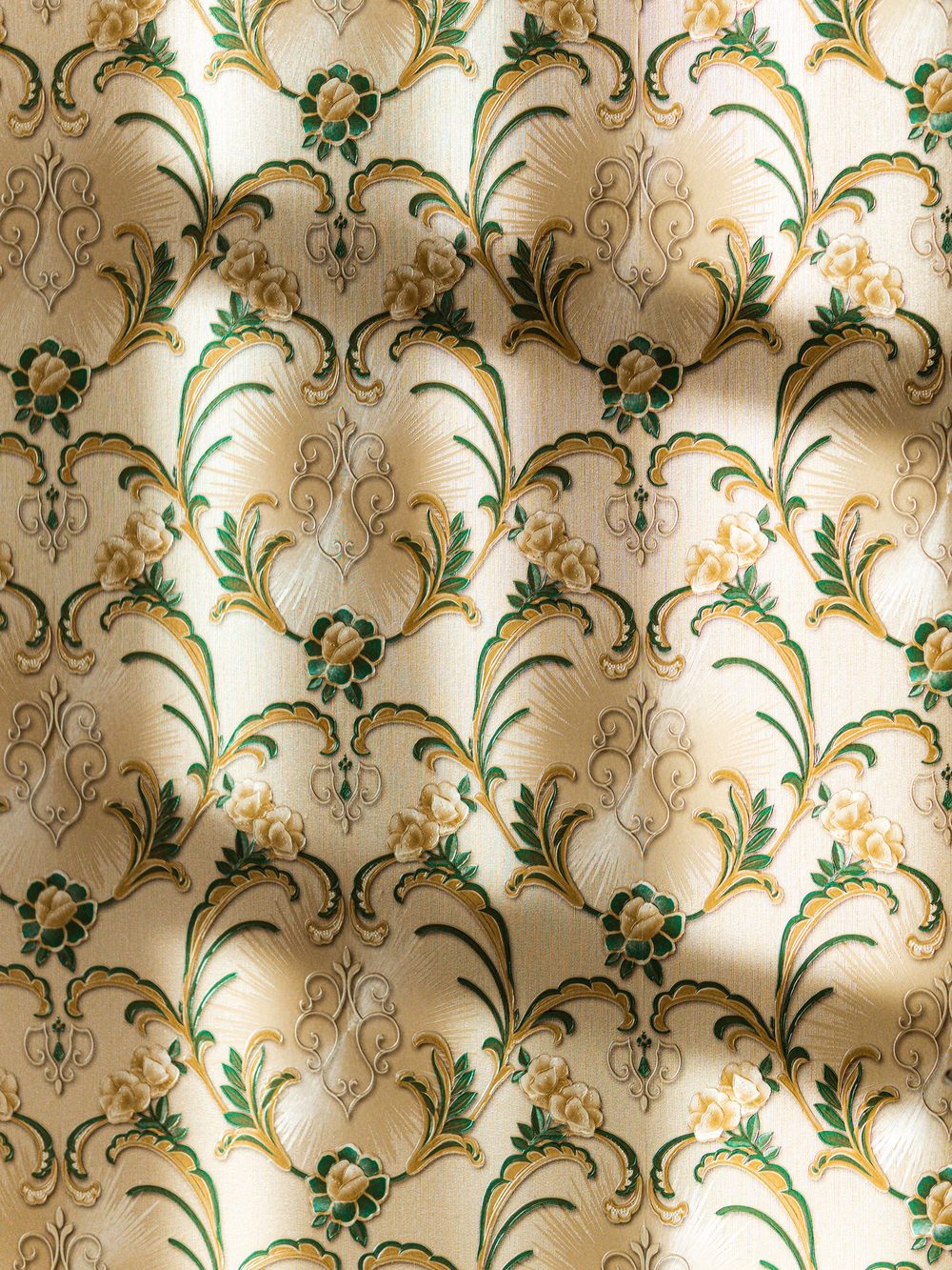 Close-up of cream wallpaper with an art nouveau floral pattern in green and gold