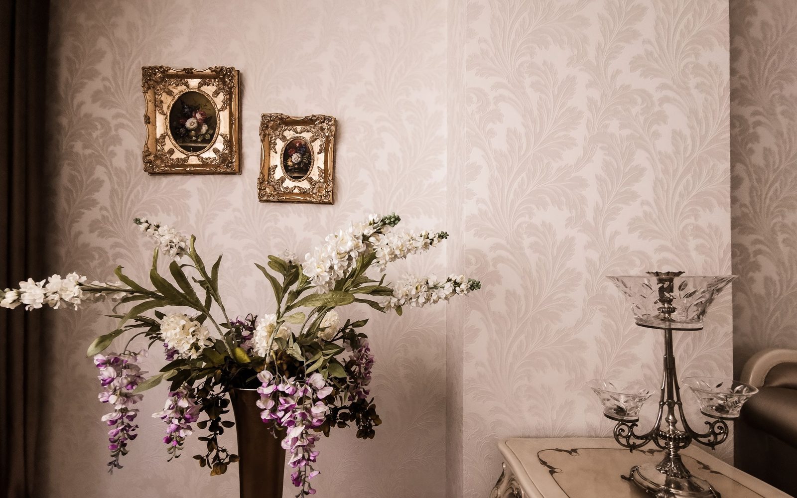 Elegant sitting room with soft parchment damask wallpaper, gilt-framed floral paintings, and a spray of orchids on a console table